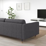 Modernes graues LANDSKRONA Sofa im minimalistischen Wohnzimmer. Weicher Stoff, Holzbeine, vor weißer Wand mit Fernseher und Pflanze.