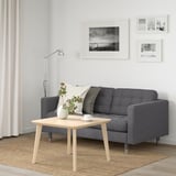 Gemütliches Wohnzimmer mit grauem Sofa, Holztisch, Lampe und Fotos. Weiße und schwarze Kissen, Blumen, leichte Vorhänge und beige Teppiche.