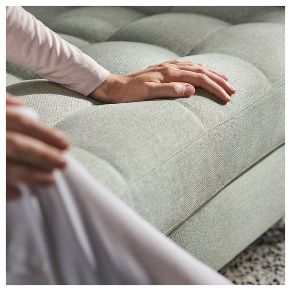 Person testet ein hellgrünes, gepolstertes Sofa, wobei der Schwerpunkt auf Komfort und Halt liegt.