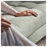 Person testet ein hellgrünes, gepolstertes Sofa, wobei der Schwerpunkt auf Komfort und Halt liegt.