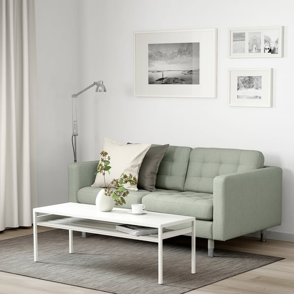 Modernes Wohnzimmer mit LANDSKRONA-Sofa, Couchtisch, grauem Teppich und Wandkunst. Gestylt mit Kissen, Vase und Ästen.