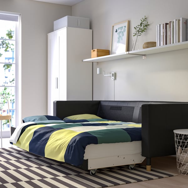 Modernes Schlafzimmer mit LANDSKRONA-Schlafsofa mit dicken Leder- und Stoffpolstern, Stauraum und einem Bücherregal mit Dekorationsgegenständen.