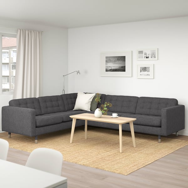 Modernes Wohnzimmer mit grauem L-förmigem Sofa, hölzernem Couchtisch, weißem Teppich und Schwarz/Weiß-Fotos.