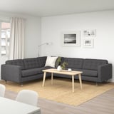 Modernes Wohnzimmer mit grauem L-förmigem Sofa, hölzernem Couchtisch, weißem Teppich und Schwarz/Weiß-Fotos.