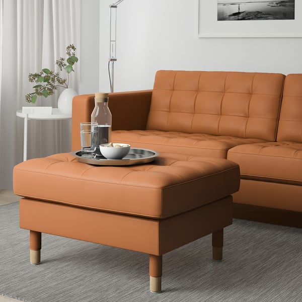 Orangefarbener Fußhocker & Couch im Wohnzimmer mit Tablett, Lampe, Pflanze.