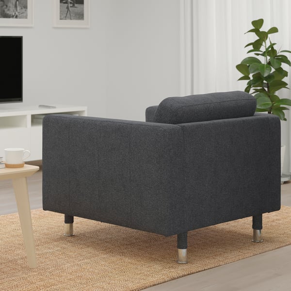 Sessel aus dunklem Stoff auf Holzbeinen, neben einem kleinen Tisch mit einer Tasse, in einem Wohnbereich.