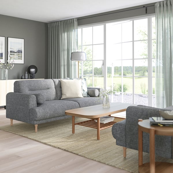 Modernes Wohnzimmer mit grauem LÅNGARYD-Sofa, Couchtisch, Beistelltisch, großem Fenster, Teppich, Sessel und Lampe.