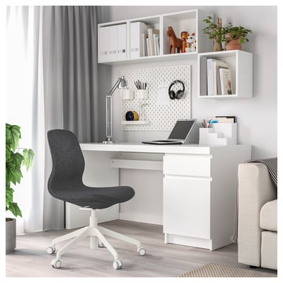 Moderne Home-Office-Einrichtung: weißer Schreibtisch, schwarzer Stuhl, Regale mit Dekor, Laptop, Lampe, Stecktafel.