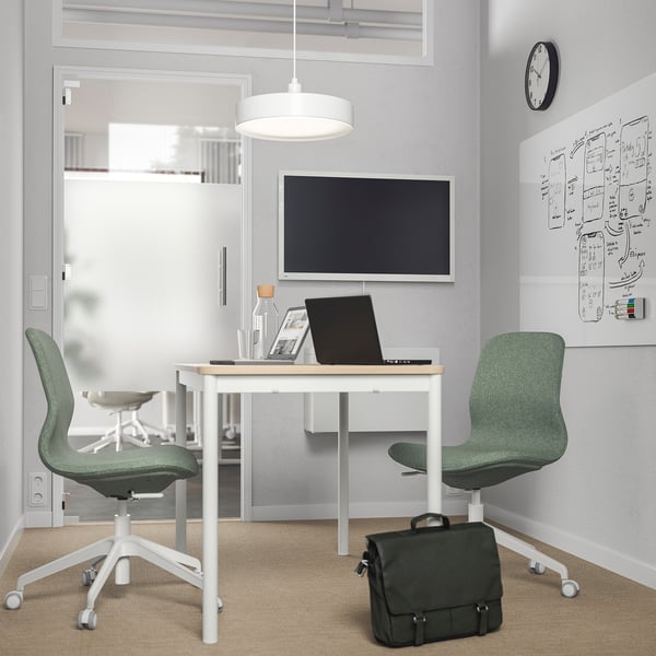 Moderne Büroräume mit weißen Schreibtischen, grünen Stühlen, digitalem Board und Hängelampe. Bürotaschen unter dem Schreibtisch.