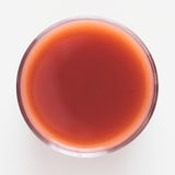 Eine Schale aus klarem Glas, gefüllt mit einem dicken, roten Beeren-Frucht-Smoothie mit glänzender Textur. Frische Erdbeeren, Himbeeren und Heidelbeeren hervorgehoben.