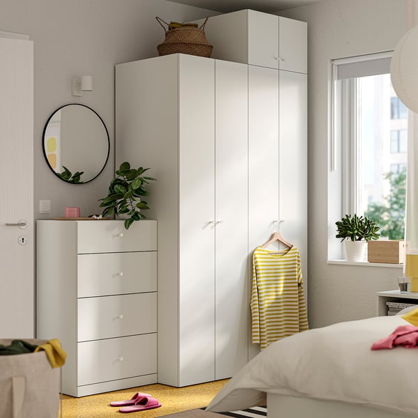Modernes Schlafzimmer mit weißen LASTARE-Möbeln . Kleiderschrank, Brust, Spiegel, Pflanze, gelbes Hemd, Bett, rosa Hausschuhe.