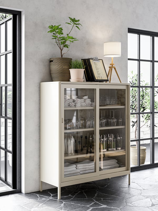 Moderner Schrank mit Glastüren, Aufbewahrungsgläsern und Handtüchern, gekrönt mit einer Pflanze und einer Lampe aus einer recycelten PET-Flasche.