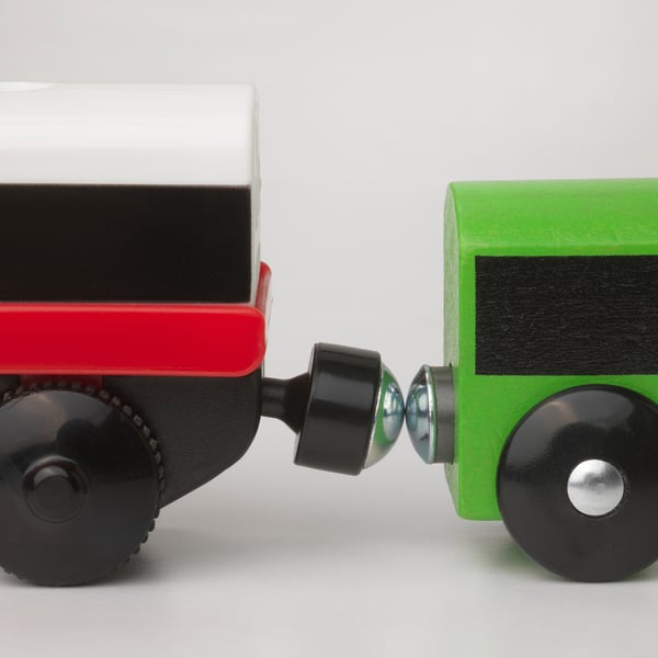 Kinderlokomotive aus Holz, rot und grün, verbunden mit einer schwarzen Kupplung, auf weißer Oberfläche.