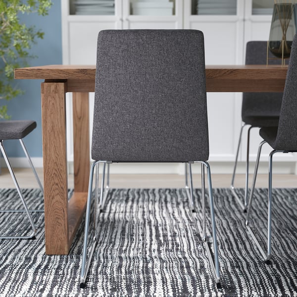 Moderne Esseinrichtung mit grau gepolsterten Stühlen mit beschichteten Kufengestellen um einen schlanken Holztisch auf einem gemusterten Teppich.