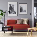 Modernes Wohnzimmer mit rotem LILLEHEM-Sofa, Kissen, schwarzem Couchtisch, Pflanze, Lampe und Fotos an grauer Wand.