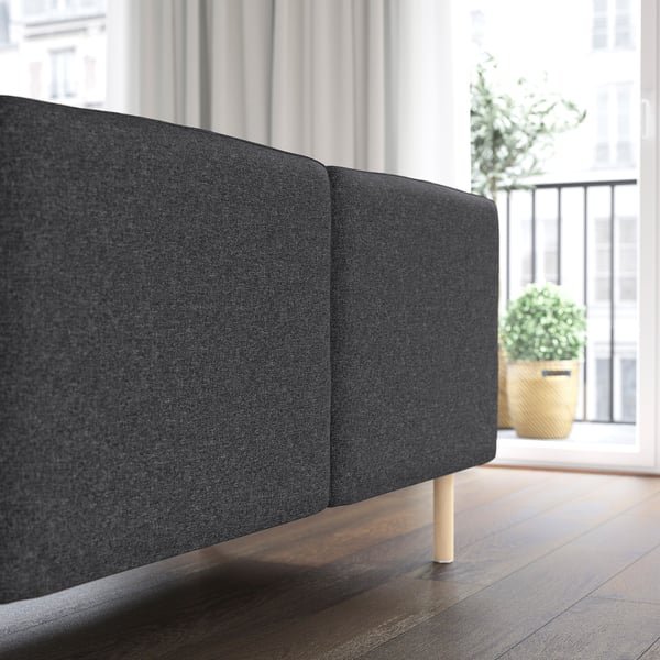 Dunkelgraues modulares Sofa mit Holzbeinen, das in der Nähe eines Fensters mit einer Topfpflanze positioniert ist. Das Sofa ist für eine individuelle Anpassung und einfache Reinigung konzipiert.