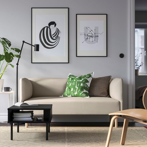 Modernes Wohnzimmer mit beigem Sofa, grünen Kissen, abstrakter Kunst, Pflanze, Büchern, Stuhl.