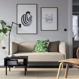 Modernes Wohnzimmer mit beigem Sofa, grünen Kissen, abstrakter Kunst, Pflanze, Büchern, Stuhl.