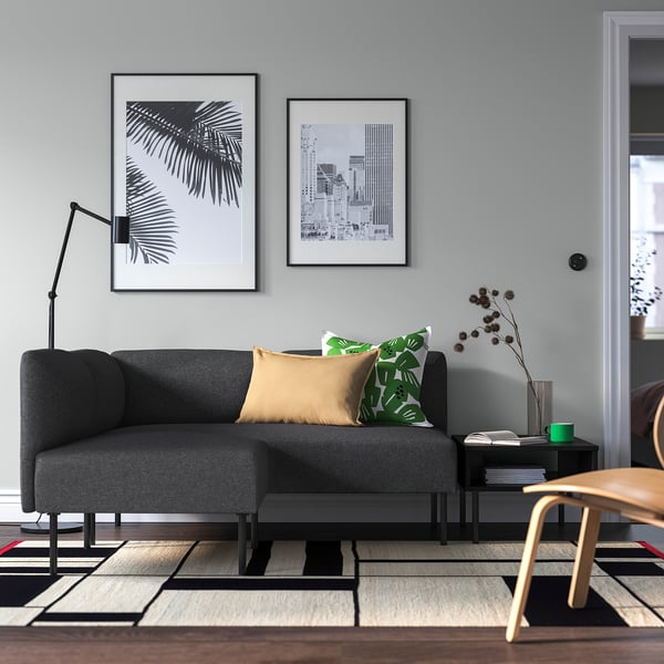 Graues Sofa, Kunst, Holzstuhl, grüne Kissen, Teppich, Stehlampe.
