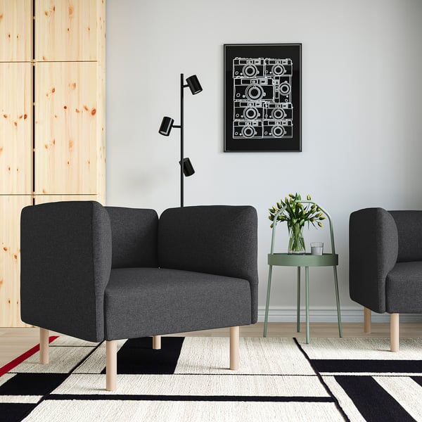 Modernes Wohnzimmer mit grauem LILLEHEM-Sofa, schwarzem Poster, schwarzer Lampe und grünem rundem Tisch mit Blumen. Grauer Teppich darunter.