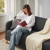 Frau liest auf Couch mit Kissen und Decke.