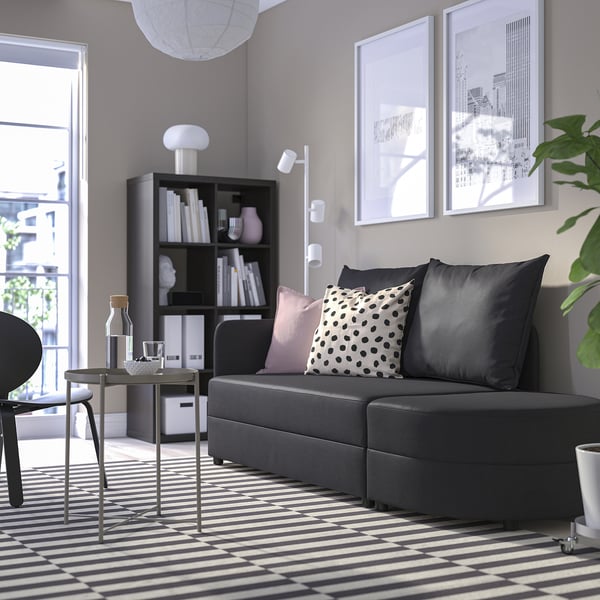 Modernes Wohnzimmer mit grauem LINDÅKRA-Schlafsofa, gemustertem Teppich, Bücherregal, Couchtisch und Dekor.