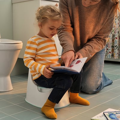 Mädchen lernt mit Hilfe von Erwachsenen auf die Toilette zu gehen.