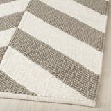 Ein handgewebter Wollteppich mit grauen und beigen Streifen, die seine weiche, hochwertige Textur betonen.