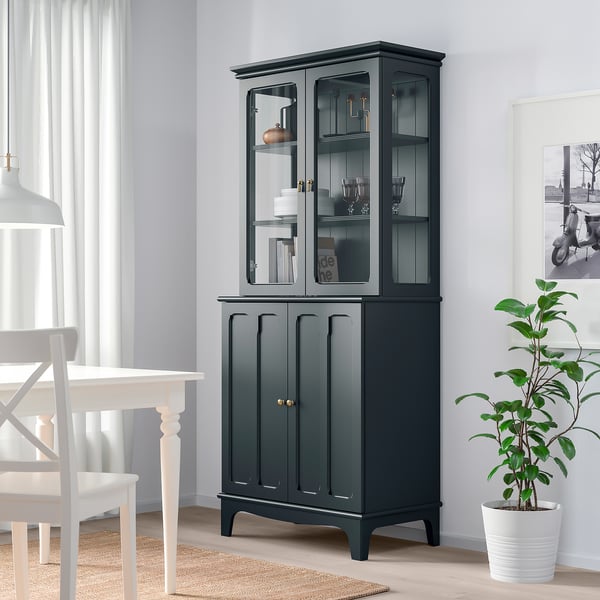 Grüner Schrank mit Glastüren im Esszimmer, neben Pflanze und Tisch.