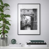 Eine gerahmte schwarz-weiße Brücke über den Kanal hängt an der Wand neben einer Topfpflanze, mit Büchern und einem Globus auf dem Regal darunter.