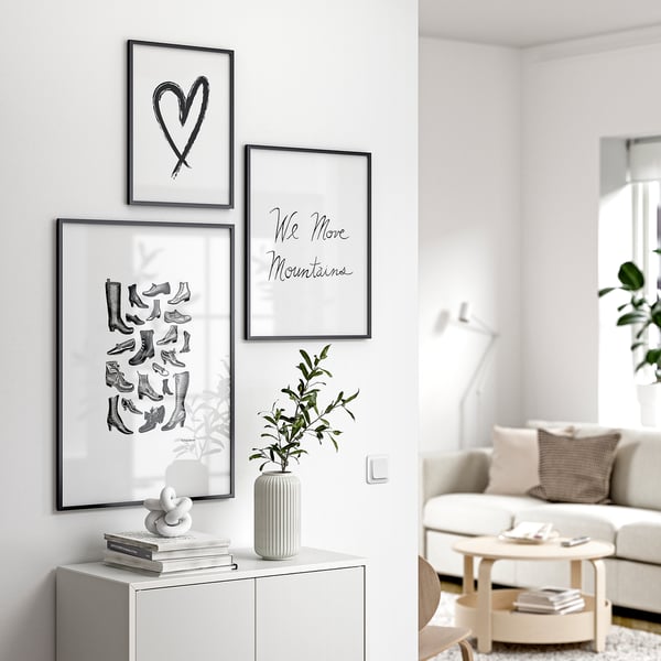 Modernes Wohnzimmer mit weißen Möbeln, drei gerahmten Kunstwerken: Herz, Stiefel, Berge und Pflanzendekoration.