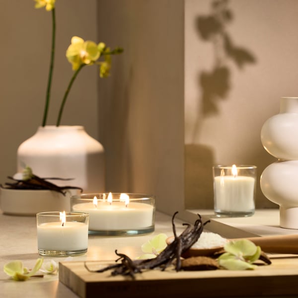 Weiße Vanillekerzen aus Glas, verschiedene Größen, Holztisch mit Orchideen.