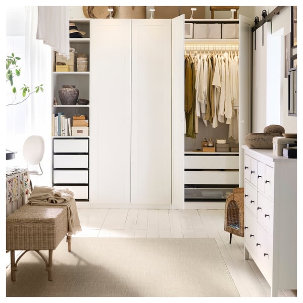 Modernes weißes Schlafzimmer mit beigem LUFTFARTYG-Teppich, Korbbank, Lampe, Kleiderschrank und Kommode mit Steinen und Korb, aufgehellt durch durchsichtige Vorhänge.