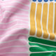 Bunte, abstrakte Muster auf einem Stoff, wahrscheinlich einem Textilprodukt, mit leuchtenden Rosa-, Grün-, Gelb- und Blautönen.