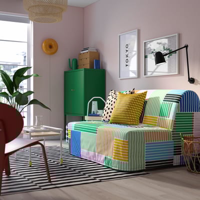 Bunt gestreiftes Schlafsofa mit verschiedenen Kissen, Zweisitzer, moderner Teppich, grüner Schrank und Wandkunst.