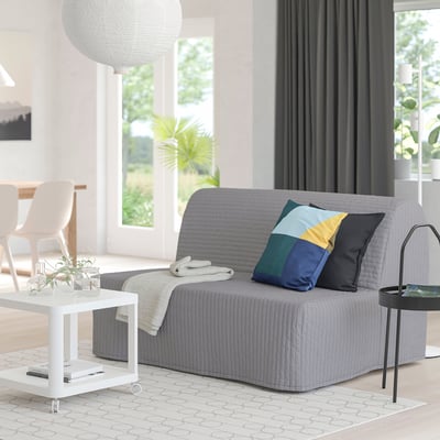 Stilvolles Wohnzimmer mit grauem Sofa, bunten Kissen, weißem Tisch, Büchern, Pflanzen.