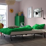 Gemütliches Schlafzimmer mit rosa Wänden, grüner Bettwäsche und einem ausklappbaren Bett, das sich vom Sofa in ein Doppelbett verwandelt, ideal für Gäste.