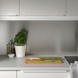 Minimalistische graue Küchentheke. Kleine Topfpflanze, Ölflaschen, Messer, Frühlingszwiebeln und Schneidebrett mit LYSEKIL Wandpaneel.