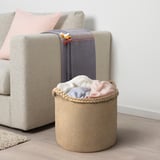 MÄVINN Jutekorb, beige, in der Nähe einer Stoffliege, nimmt gefaltete Decken auf. Griffe für den Transport, passt gut in den Wohnraum.