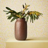 Vase zeigt Blumen auf Ständer vor gemusterter Wand.
