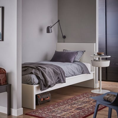Modernes Schlafzimmer mit einem weißen MALM-Bett mit grauer Bettwäsche, einer an der Wand montierten schwarzen Lampe und Holzboden; Minimalistisch und gemütlich.