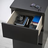 Öffnen Sie die schwarze Schublade der MALM-Truhe, in der Uhr, Bücher, Schlüssel und Schachtel aufbewahrt werden.