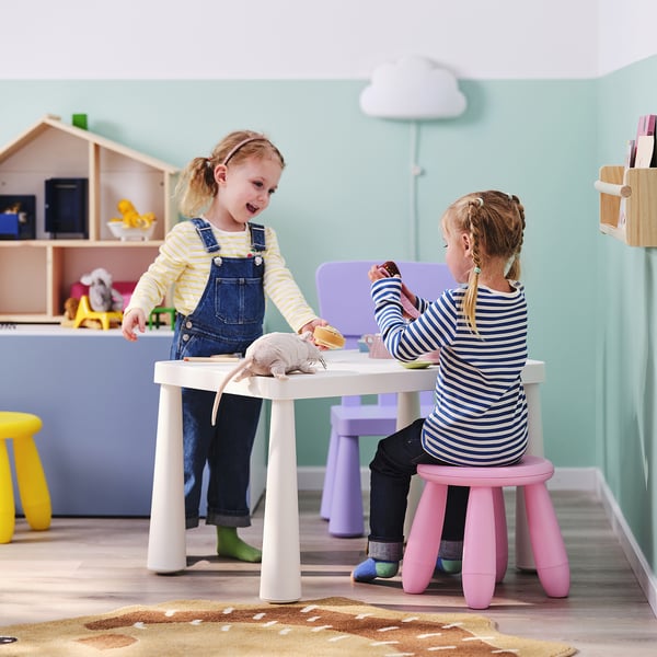 Zwei Kinder, die mit kleinen Möbeln in einem hellen, farbenfrohen Raum spielen. Oder Kinder, die in einem bunten Raum mit Spielzeugmöbeln spielen.
