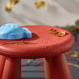 Roter Kinderhocker mit blauem Spielzeug und Blättern, draußen