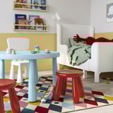 Kinderspielbereich mit blauem Tisch, roten Hockern. Heller Teppich, weißer Stuhl.