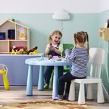 Kinder spielen mit Spielzeug am blauen Tisch, Küche im Hintergrund.