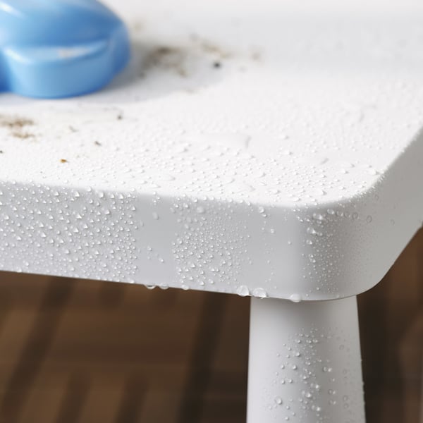 Wassertropfen perlen auf weißer Kindertischkante für den Außenbereich. Der blaue Gegenstand sitzt auf dem Tisch. Perfekt für Picknicks.