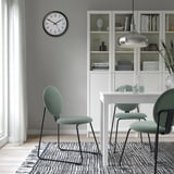 Moderne Esseinrichtung mit MÅNHULT-Stühlen, Uhr und Bücherregal mit grünen gepolsterten Stühlen und dekoriertem Bücherregal.