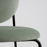 Nahaufnahme eines modernen, gepolsterten Stuhls mit weichem, grünem Stoff auf rundem Sitz und Rückenlehne, der von einem schlanken, schwarzen Metallgestell getragen wird.