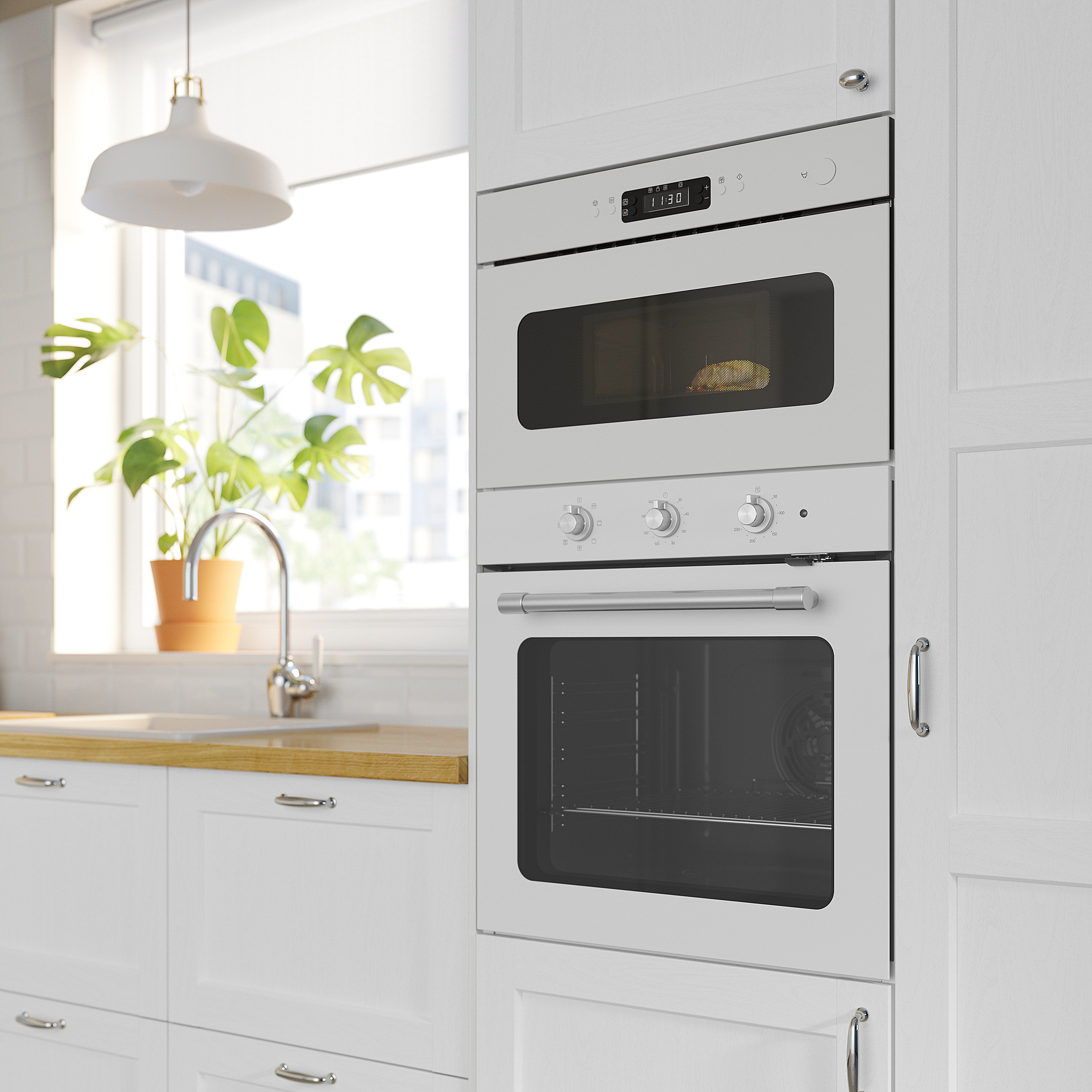 Moderne Küche mit weißem eingebautem Doppelofen, Digitalanzeige auf dem Backofen, minimalistischem Design; Topfpflanze am Fenster.
